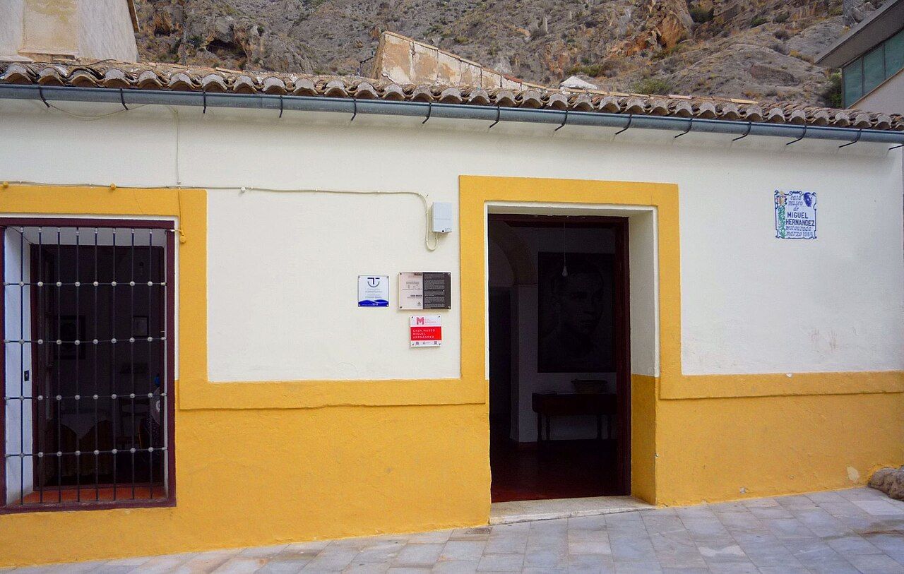 Fachada blanca y ocre de la Casa-Museo de Miguel Hernández en Orihuela, con la sierra rocosa detrás