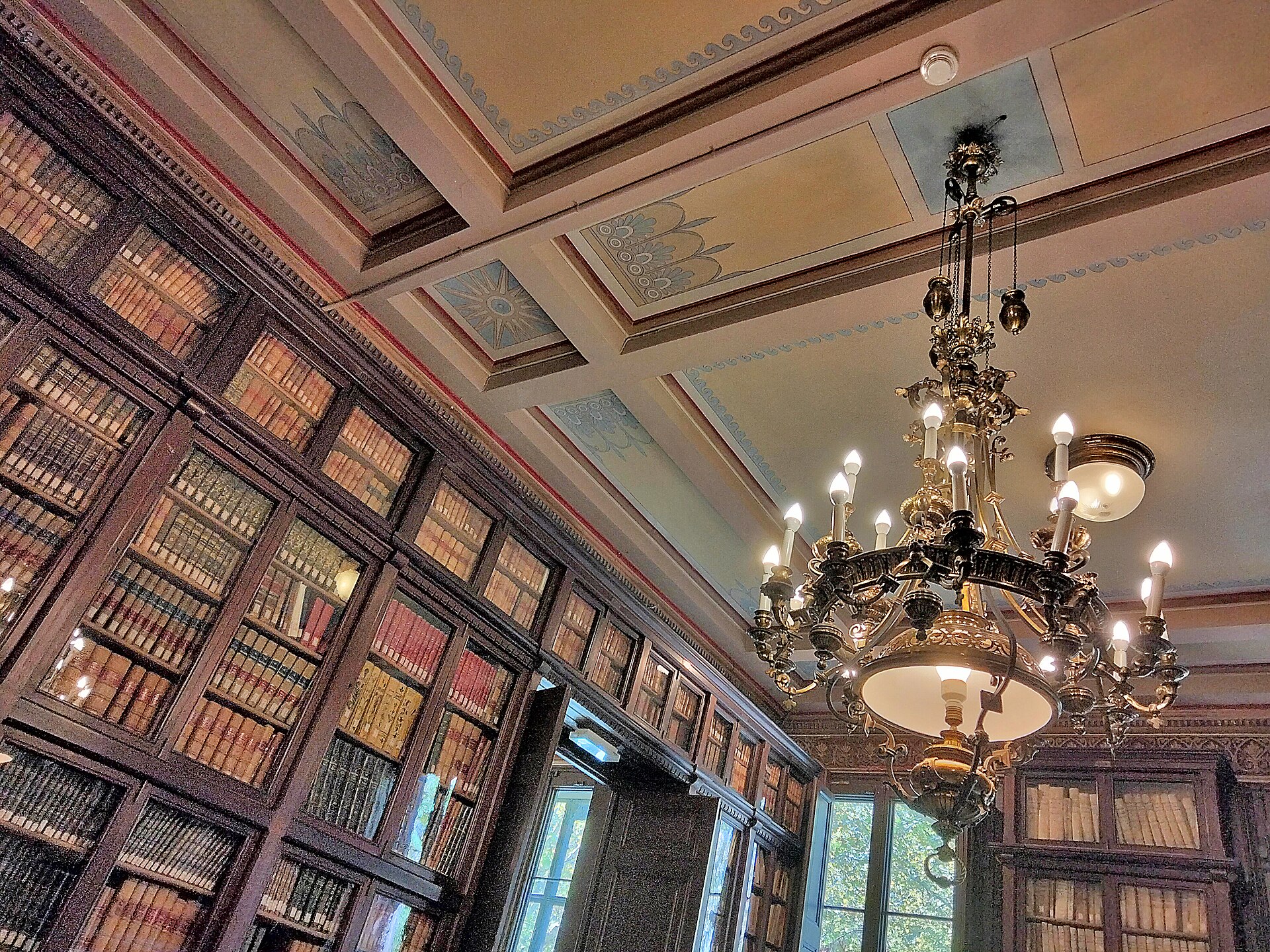 Techo y lámpara de araña de la sala de actos de la Biblioteca Pública Arús, en Barcelona, rodeada de estanterías de madera
