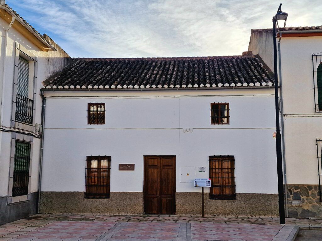 Fachada encalada de la Casa de Bernarda Alba en Valderrubio, con puerta de madera y ventanas con rejas