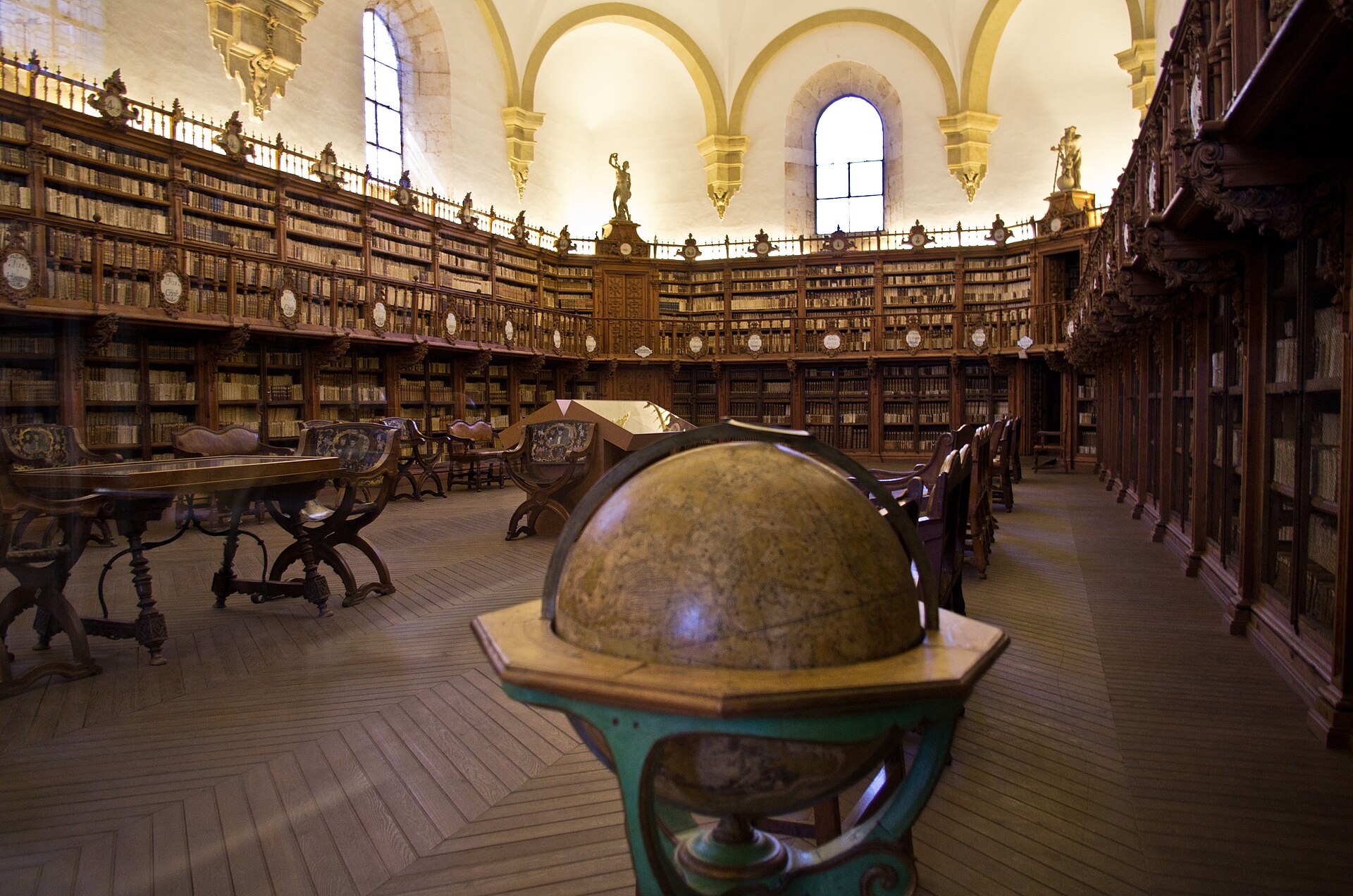 Sala de la Biblioteca Histórica de la Universidad de Salamanca, con un globo terráqueo en primer plano y estanterías de madera en dos alturas
