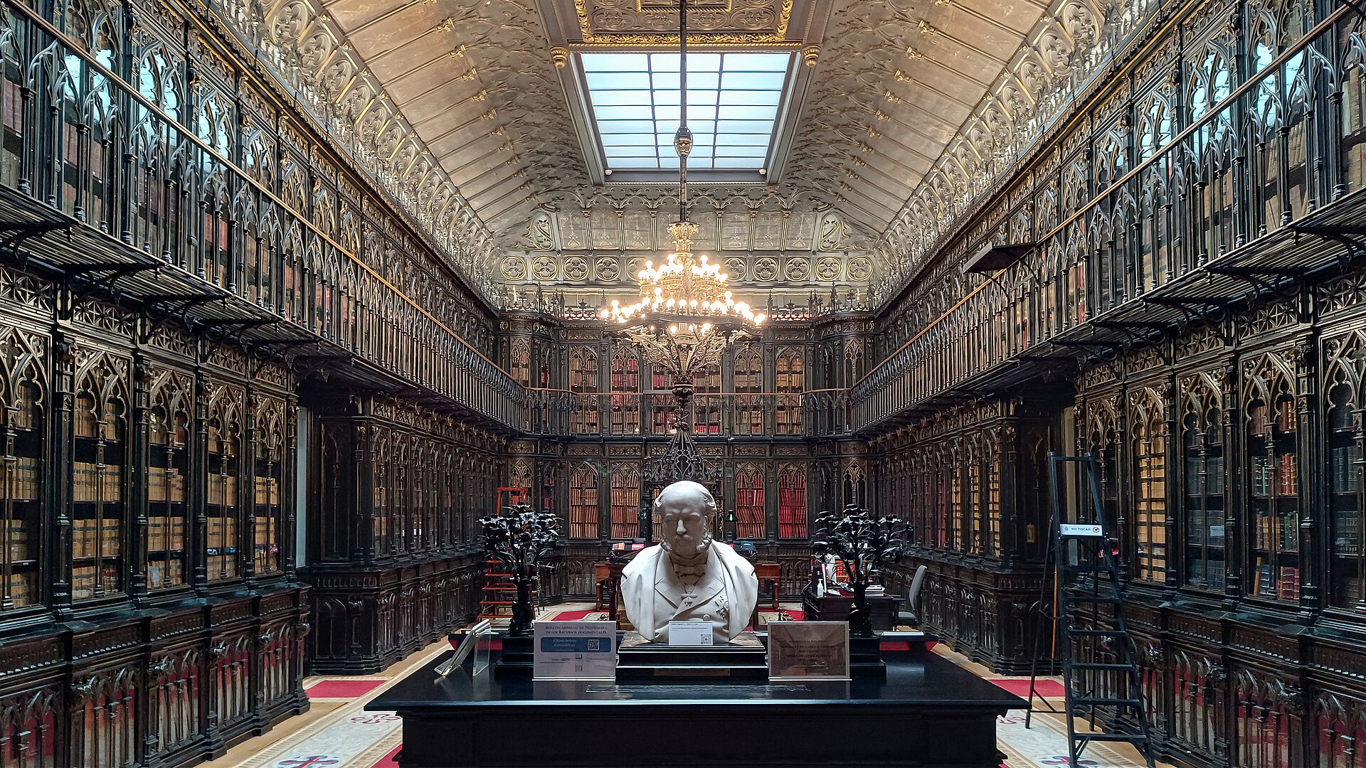 Biblioteca del Palacio del Senado, en Madrid, con estanterías en dos alturas, lámpara de araña, lucernario y un busto en el centro