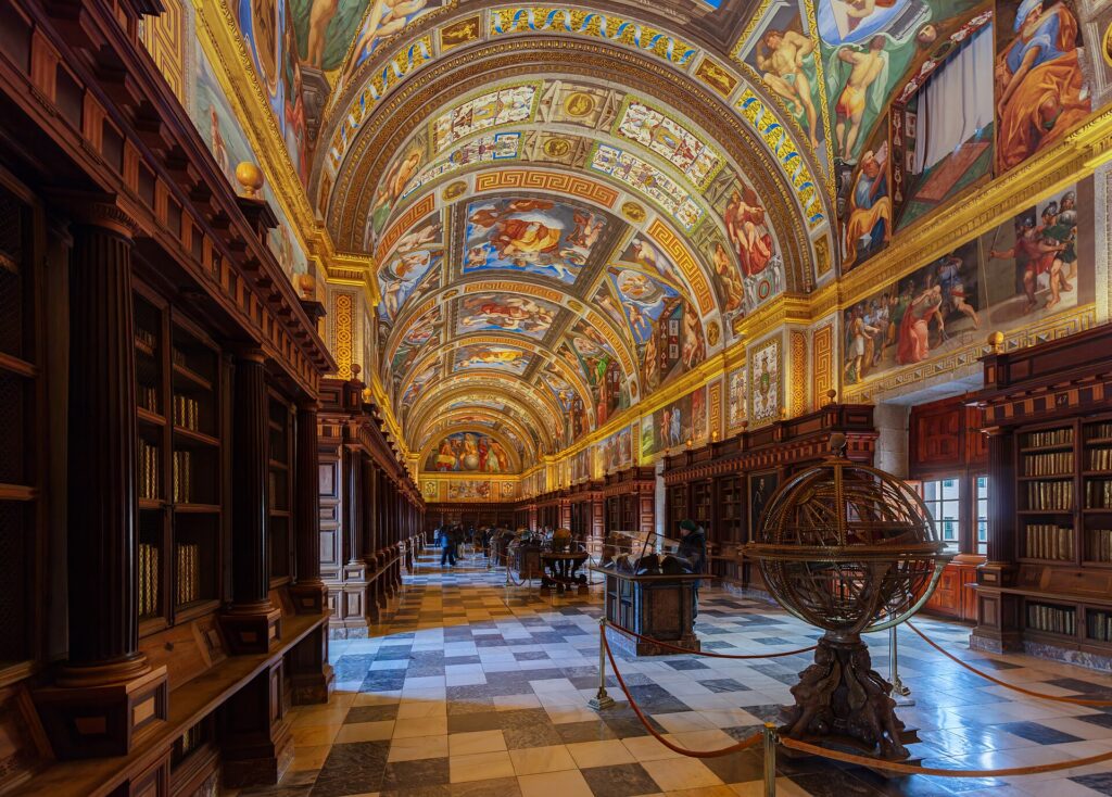 Salón Principal de la Real Biblioteca de El Escorial, con la bóveda pintada al fresco, estanterías de madera a ambos lados y una esfera armilar en el centro