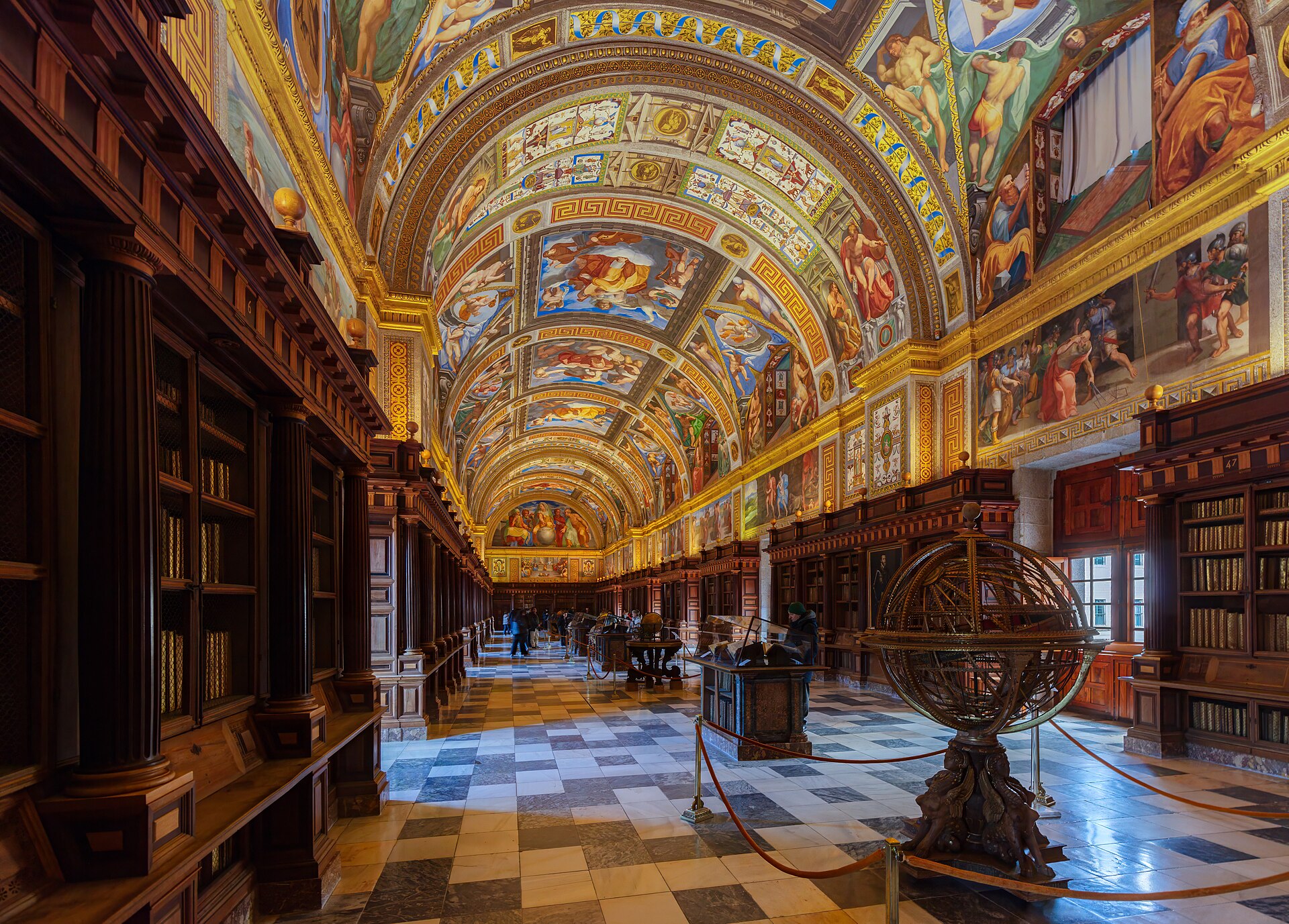 Salón Principal de la Real Biblioteca de El Escorial, con la bóveda pintada al fresco, estanterías de madera a ambos lados y una esfera armilar en el centro