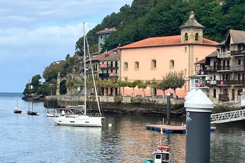 La bahía de Pasaia, con un edificio rosado con campanario junto al agua y un velero fondeado