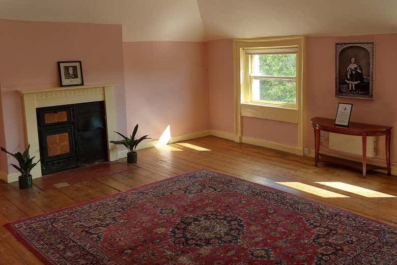 Habitación infantil de Oscar Wilde en el último piso de su casa de Dublín, con paredes rosas, chimenea y una alfombra roja sobre el suelo de madera