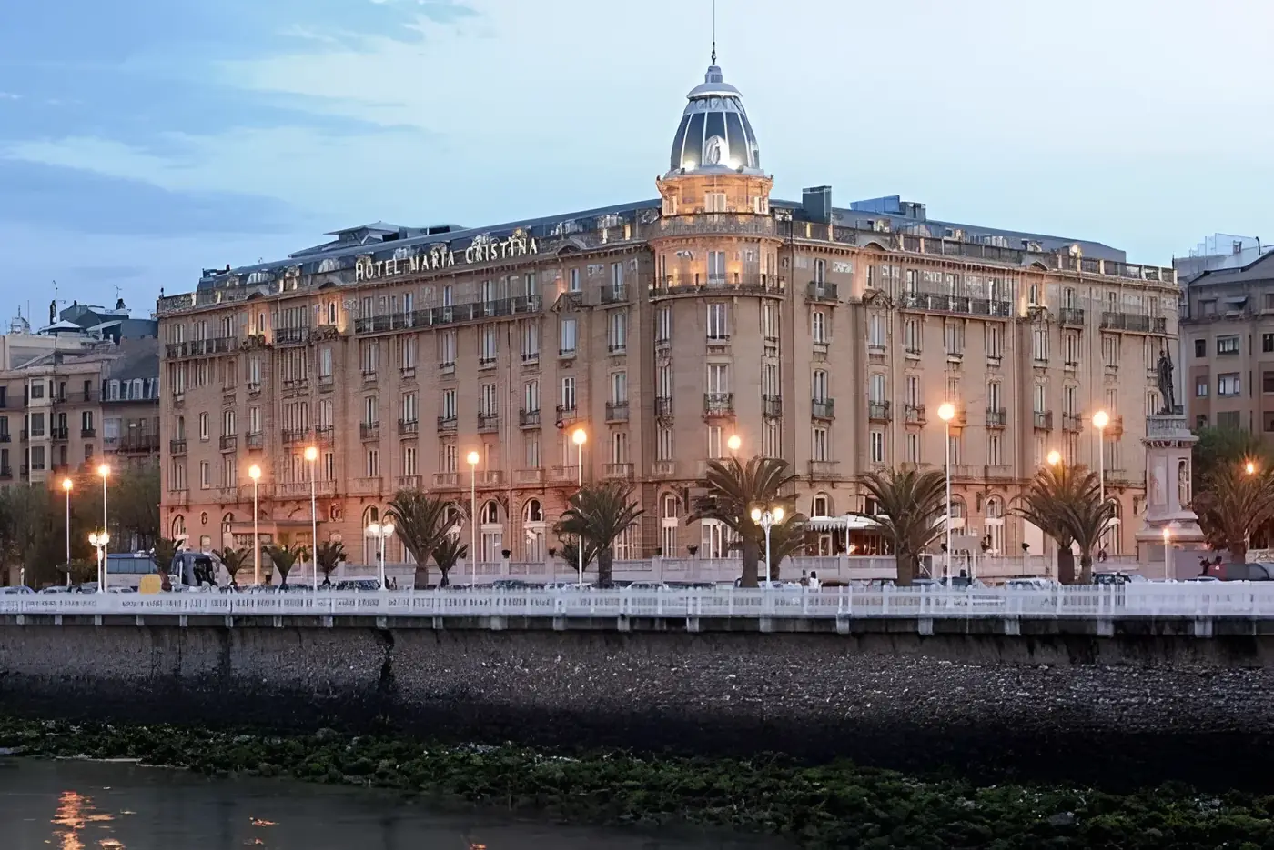 Hotel María Cristina de San Sebastián iluminado al atardecer, junto a la ría del Urumea