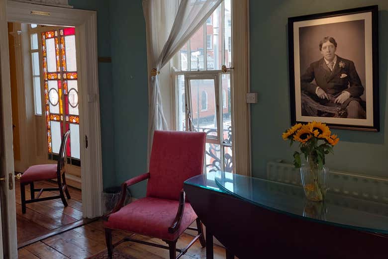 Sala de la casa de Oscar Wilde en Merrion Square, Dublín, con un retrato del escritor en la pared, girasoles sobre una mesa y una vidriera al fondo