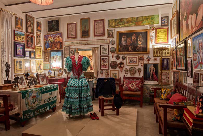Sala del Palacio de las Dueñas con las paredes llenas de cuadros y carteles y un traje de flamenca en el centro